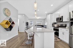 The kitchen features white cabinetry, stainless steel appliances, a white subway tile backsplash, and a large island with a light-colored countertop and seating - 