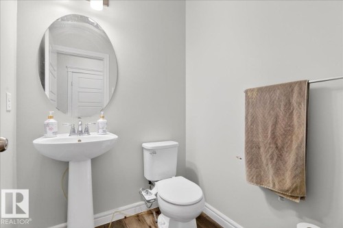 This bathroom features a white pedestal sink with a chrome faucet, an oval mirror, and a toilet - 203 Cavanagh Common, Edmonton, AB - Indoor Photo Showing Bathroom