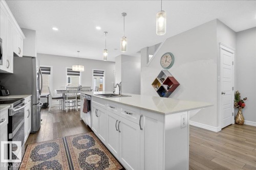The kitchen features white cabinetry, stainless steel appliances, and a central island with a light-colored countertop - 203 Cavanagh Common, Edmonton, AB - Indoor Photo Showing Kitchen With Upgraded Kitchen