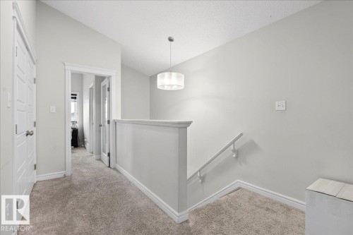 The property features a staircase with a white handrail and a landing with plush carpeting - 203 Cavanagh Common, Edmonton, AB - Indoor Photo Showing Other Room