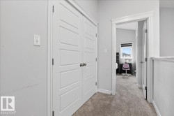 Hallway featuring light gray walls, white trim, and a textured gray carpet - 