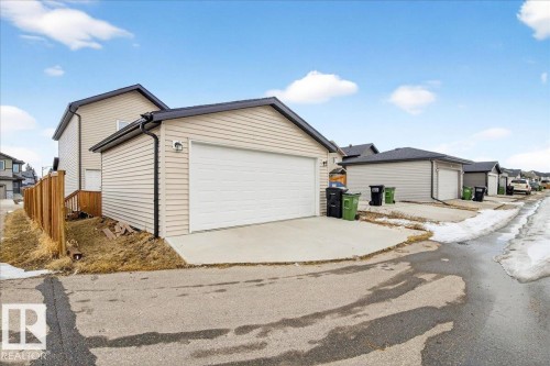 The property features a detached garage with a white garage door, concrete driveway, and light-colored siding - 203 Cavanagh Common, Edmonton, AB - Outdoor With Exterior
