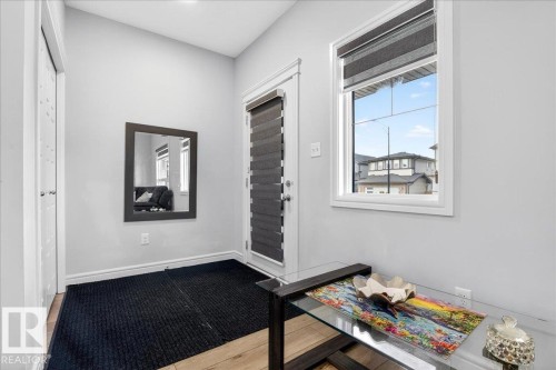 This entry area features light wood flooring, a window providing natural light, and a white door with a window blind - 203 Cavanagh Common, Edmonton, AB - Indoor Photo Showing Other Room