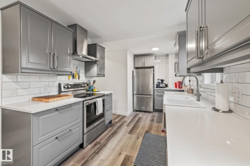The kitchen features gray cabinetry, white countertops, and stainless steel appliances, including a range and a refrigerator - 9321 92 Street, Edmonton, AB - Indoor Photo Showing Kitchen With Stainless Steel Kitchen