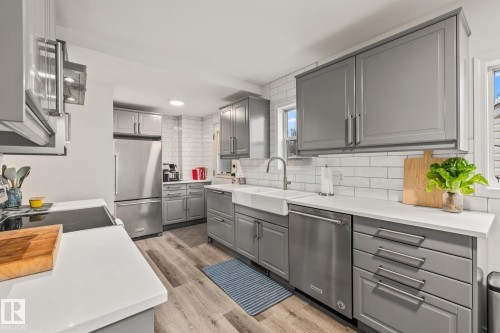 The kitchen features gray cabinetry with stainless steel hardware, white countertops, and a white subway tile backsplash - 9321 92 Street, Edmonton, AB - Indoor Photo Showing Kitchen With Stainless Steel Kitchen
