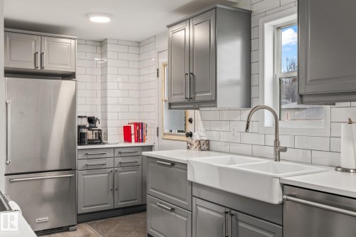 The kitchen features a stainless steel refrigerator, grey cabinetry, white subway tile backsplash, and a double basin farmhouse sink with a gooseneck faucet - 9321 92 Street, Edmonton, AB - Indoor Photo Showing Kitchen With Double Sink With Upgraded Kitchen