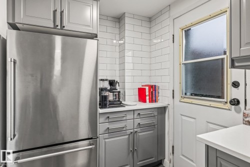 The kitchen features stainless steel appliances, grey cabinetry, white countertops, and a white subway tile backsplash - 9321 92 Street, Edmonton, AB - Indoor Photo Showing Other Room