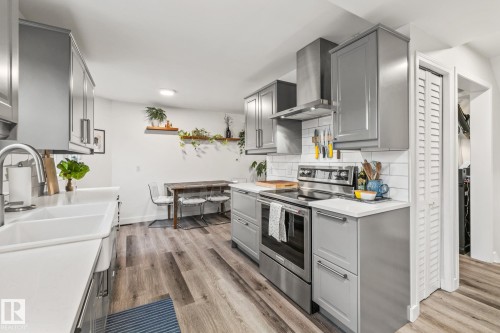 The kitchen features grey cabinetry, white countertops, a stainless steel oven and range hood, and light wood-style flooring - 9321 92 Street, Edmonton, AB - Indoor Photo Showing Kitchen