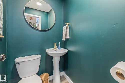 Well-appointed bathroom featuring a pedestal sink with a gold-tone faucet, a wall-mounted circular mirror, and a toilet - 9321 92 Street, Edmonton, AB - Indoor Photo Showing Bathroom