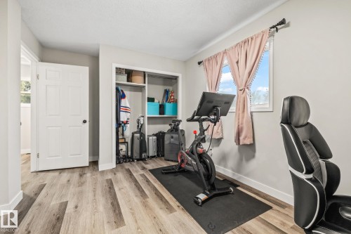 This room features light-colored walls, wood-style flooring, a window with curtains, and an open closet space with shelving - 9321 92 Street, Edmonton, AB - Indoor Photo Showing Gym Room