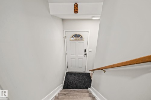 Entryway featuring a white door with an arched window, a natural wood handrail, and light-colored flooring - 9321 92 Street, Edmonton, AB - Indoor Photo Showing Other Room