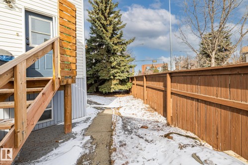 The property features a private fenced yard with a concrete pathway and a mature evergreen tree - 9321 92 Street, Edmonton, AB - Outdoor