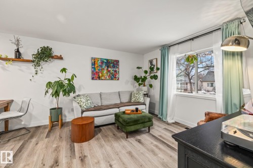 This living area features light-colored flooring, a large window with light-colored curtains, and white walls - 9321 92 Street, Edmonton, AB - Indoor Photo Showing Living Room
