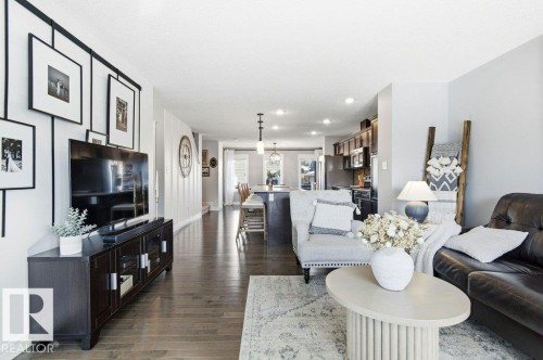 This inviting living space features hardwood floors, a light-colored area rug, and an open layout providing sightlines to the kitchen and dining areas - 16720 15 Avenue, Edmonton, AB - Indoor Photo Showing Living Room