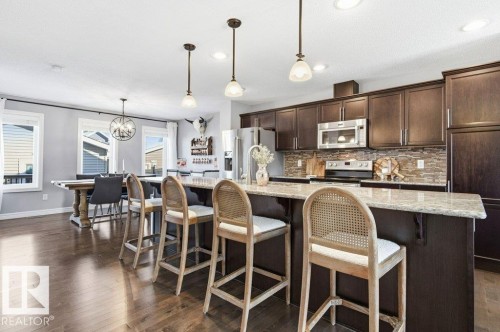 Spacious kitchen featuring dark wood cabinetry, stainless steel appliances, a stone tile backsplash, and a large island with a light-colored countertop - 16720 15 Avenue, Edmonton, AB - Indoor