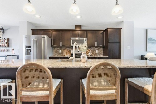 The kitchen features dark wood cabinetry, stainless steel appliances, and a tiled backsplash - 16720 15 Avenue, Edmonton, AB - Indoor Photo Showing Kitchen