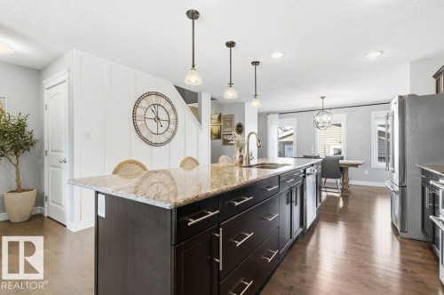 The kitchen features an expansive island with granite countertops, a built-in sink, and pendant lighting - 16720 15 Avenue, Edmonton, AB - Indoor Photo Showing Kitchen With Upgraded Kitchen