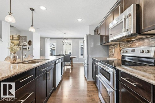The kitchen features dark wood cabinetry, granite countertops, and stainless steel appliances including a refrigerator, microwave, and oven - 16720 15 Avenue, Edmonton, AB - Indoor Photo Showing Kitchen With Double Sink With Upgraded Kitchen