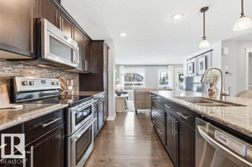 The kitchen features dark wood cabinetry, granite countertops, and stainless steel appliances including a microwave, double oven, and dishwasher - 16720 15 Avenue, Edmonton, AB - Indoor Photo Showing Kitchen With Double Sink With Upgraded Kitchen