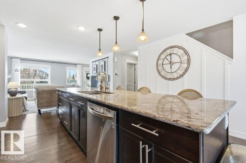 The kitchen features an island with dark cabinetry, a light-colored granite countertop, a stainless steel dishwasher, and a sink with a gooseneck faucet - 16720 15 Avenue, Edmonton, AB - Indoor Photo Showing Kitchen With Upgraded Kitchen