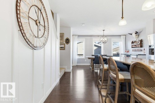 The open concept living area features dark hardwood flooring, a dining area with a modern chandelier, and a kitchen island with seating - 16720 15 Avenue, Edmonton, AB - Indoor Photo Showing Dining Room