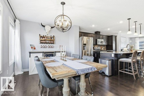 Open concept living space featuring dark hardwood flooring throughout, a dining area with a rustic-style table, and a kitchen with dark cabinetry, stainless steel appliances, and an island with seating - 16720 15 Avenue, Edmonton, AB - Indoor Photo Showing Dining Room