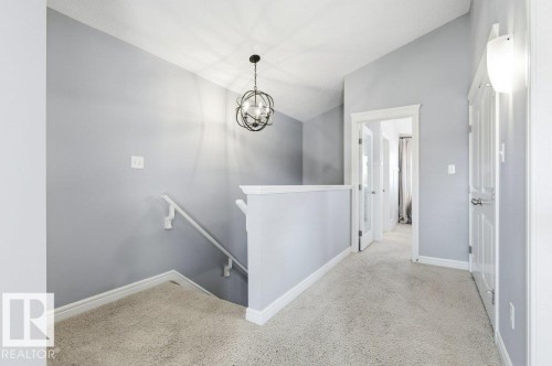 The upper landing features a modern spherical chandelier, a wall-mounted light fixture, and light-colored carpeting - 16720 15 Avenue, Edmonton, AB - Indoor Photo Showing Other Room