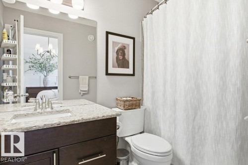 The bathroom features a vanity with a light-colored countertop and dark cabinetry, a mirror with overhead lighting, and a white shower curtain - 16720 15 Avenue, Edmonton, AB - Indoor Photo Showing Bathroom