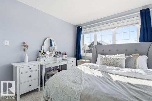 This bedroom features a large window with blue curtains, providing ample natural light - 16720 15 Avenue, Edmonton, AB - Indoor Photo Showing Bedroom