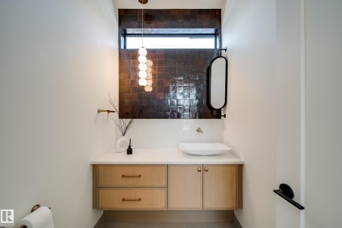 Bathroom featuring a white vessel sink, a light wood vanity with drawers and cabinets, and a unique wall-mounted mirror - 13804 85 Avenue, Edmonton, AB - Indoor