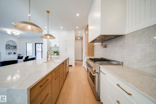 Modern kitchen featuring light hardwood floors, white countertops, two brass pendant lights, stainless steel appliances, and a marble backsplash - 13804 85 Avenue, Edmonton, AB - Indoor Photo Showing Kitchen With Upgraded Kitchen