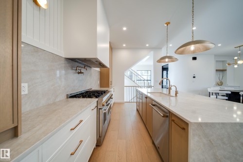 Spacious kitchen featuring an extensive island with a sink and gold-toned fixtures, a stainless steel range with a matching vent hood, and light wood flooring - 13804 85 Avenue, Edmonton, AB - Indoor Photo Showing Kitchen With Upgraded Kitchen