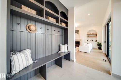 Entryway featuring built-in shelving with coat hooks and a bench, light-colored tile flooring, and light hardwood flooring visible in the adjacent room - 13804 85 Avenue, Edmonton, AB - Indoor
