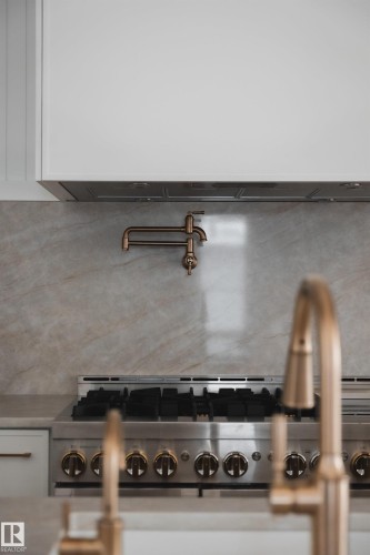 The kitchen features a stainless steel range with gold-toned knobs, a pot filler, and a marbled backsplash - 13804 85 Avenue, Edmonton, AB - Indoor Photo Showing Kitchen