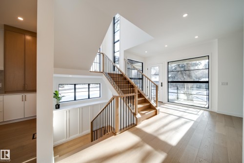 Bright foyer with natural light wood flooring, a staircase with wood treads and black metal balusters, and large windows - 13804 85 Avenue, Edmonton, AB - Indoor Photo Showing Other Room