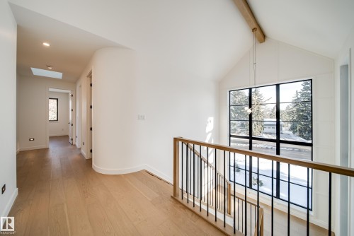 The property features light hardwood floors, a large window with black framing, and a wooden handrail with black balusters - 13804 85 Avenue, Edmonton, AB - Indoor Photo Showing Other Room