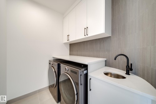 This utility room features white cabinetry, a built-in sink with a matte black faucet, and a contemporary tiled backsplash - 13804 85 Avenue, Edmonton, AB - Indoor Photo Showing Laundry Room