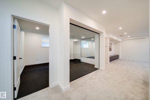 This versatile interior space features light-colored carpeting, recessed lighting, and a room with dark flooring visible through a clear glass wall - 13804 85 Avenue, Edmonton, AB - Indoor Photo Showing Other Room