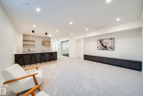 The property features a spacious room with light-colored carpeting, recessed lighting, and a built-in bar area with a light-colored countertop, dark cabinetry, and open wooden shelving - 13804 85 Avenue, Edmonton, AB - Indoor