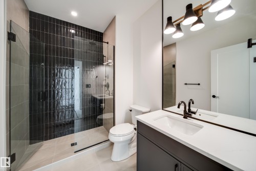 The bathroom features a spacious walk-in shower with dark tiled walls, a white vanity with a rectangular sink, and a large mirror with a four-light fixture - 13804 85 Avenue, Edmonton, AB - Indoor Photo Showing Bathroom
