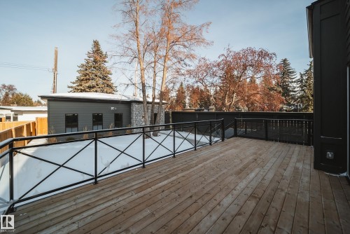 The property features a spacious wooden deck with black metal railings, overlooking a snow-covered yard and mature trees - 13804 85 Avenue, Edmonton, AB - Outdoor