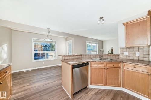 Kitchen featuring light brown cabinets, a peninsula, stainless steel dishwasher, light wood-style flooring, and decorative light fixtures - 14 Spring Gate, Spruce Grove, AB - Indoor Photo Showing Kitchen