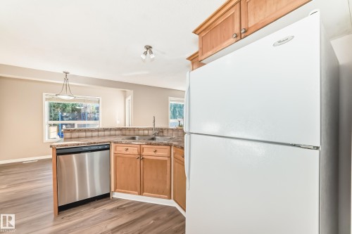 Kitchen featuring freestanding refrigerator, stainless steel dishwasher, decorative light fixtures, light wood-style flooring, and healthy amount of natural light - 14 Spring Gate, Spruce Grove, AB - Indoor Photo Showing Kitchen