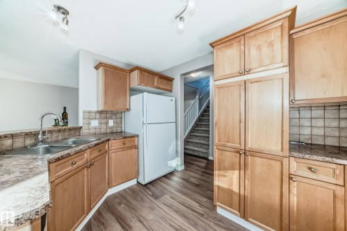 Kitchen featuring tasteful backsplash, freestanding refrigerator, light brown cabinetry, light wood-type flooring, and rail lighting - 14 Spring Gate, Spruce Grove, AB - Indoor Photo Showing Kitchen With Double Sink