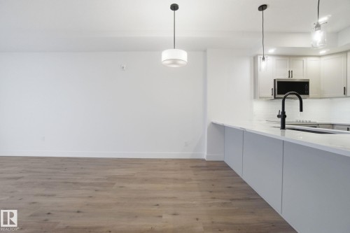 The property features hardwood floors and a kitchen with white cabinetry, a microwave, and a dark-toned faucet - 516 260 Bellerose Dr, St. Albert, AB - Indoor Photo Showing Kitchen With Upgraded Kitchen