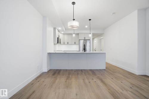 This open-concept living area features light-toned wood flooring and pristine white walls - 516 260 Bellerose Dr, St. Albert, AB - Indoor Photo Showing Kitchen With Upgraded Kitchen