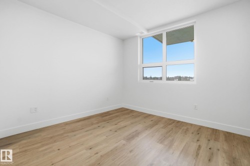 This room features light-colored flooring, white walls, and a large window providing views of the sky and distant trees - 516 260 Bellerose Dr, St. Albert, AB - Indoor Photo Showing Other Room