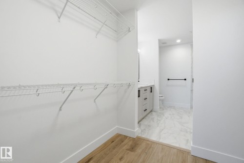 The property features a closet with wire shelving and wood-style flooring, leading into a bathroom with marble-style flooring, a vanity with drawers and a countertop, and a toilet - 516 260 Bellerose Dr, St. Albert, AB - Indoor With Storage