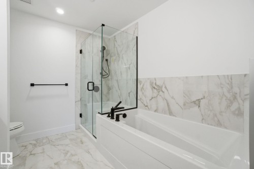 The bathroom features a combination tub and shower with a glass enclosure, white marble-style floor and wall tiles, and matte black fixtures - 516 260 Bellerose Dr, St. Albert, AB - Indoor Photo Showing Bathroom