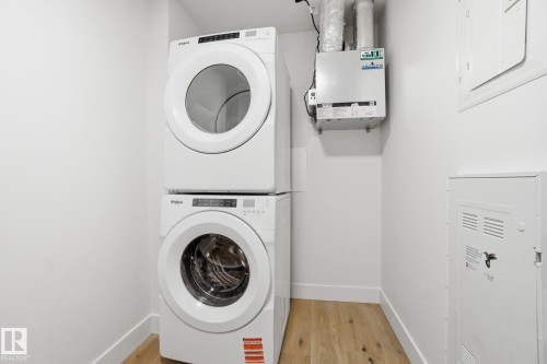 Utility area featuring a stacked washer and dryer, wood flooring, and white walls - 516 260 Bellerose Dr, St. Albert, AB - Indoor Photo Showing Laundry Room
